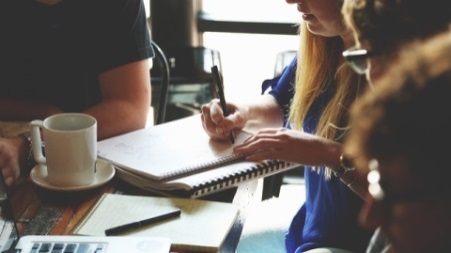 Four people sitting around a table with one woman taking notes